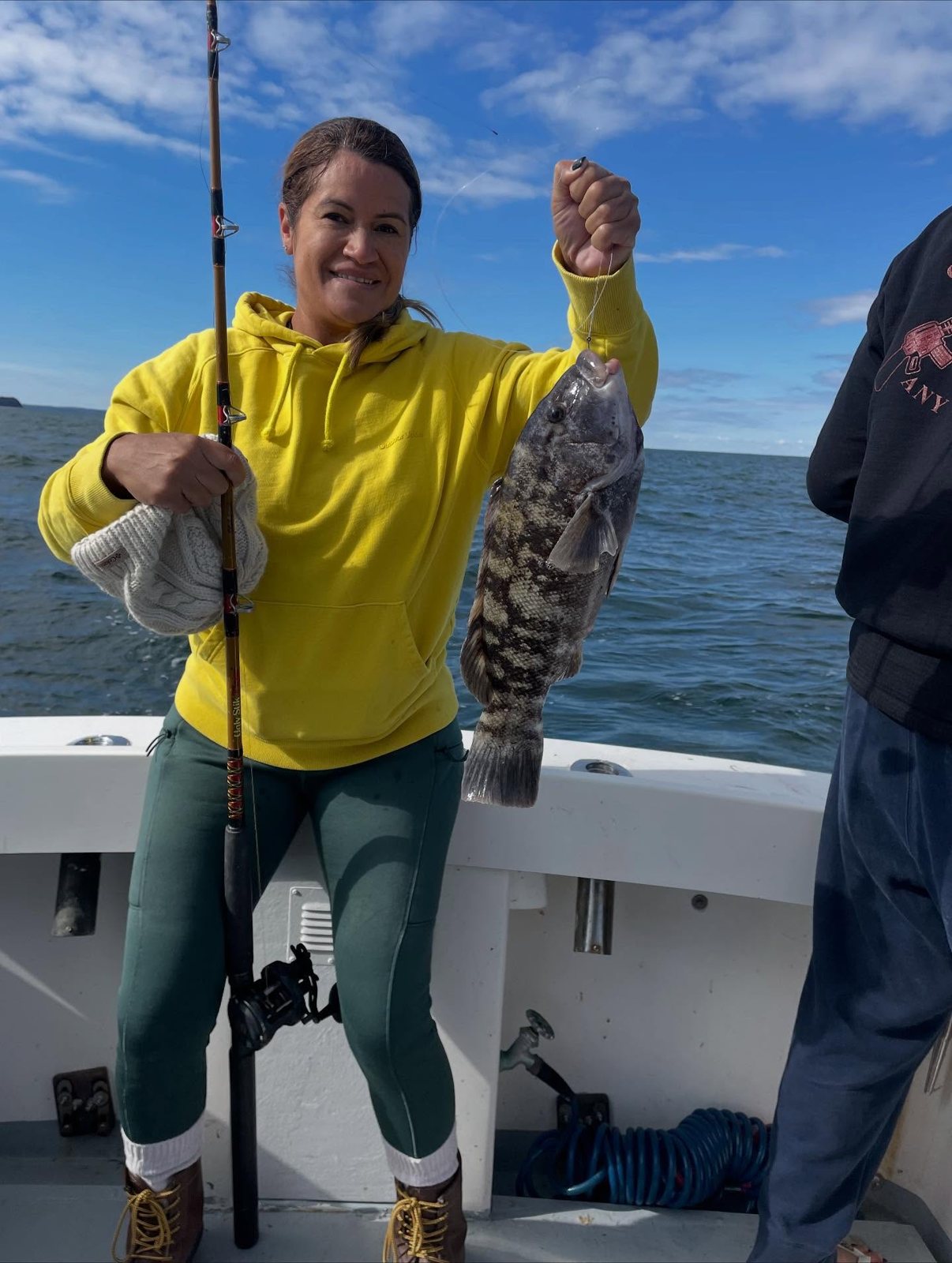 Angler in a yellow hoodie holding a blackfish caught off Mount Sinai, NY