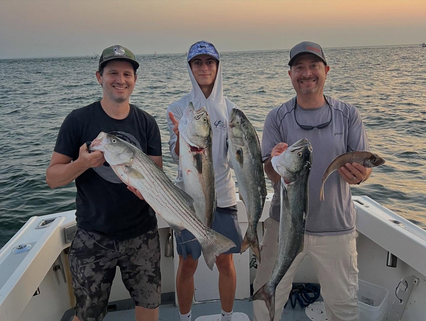 Three anglers holding striped bass on an evening Long Island Sound charter