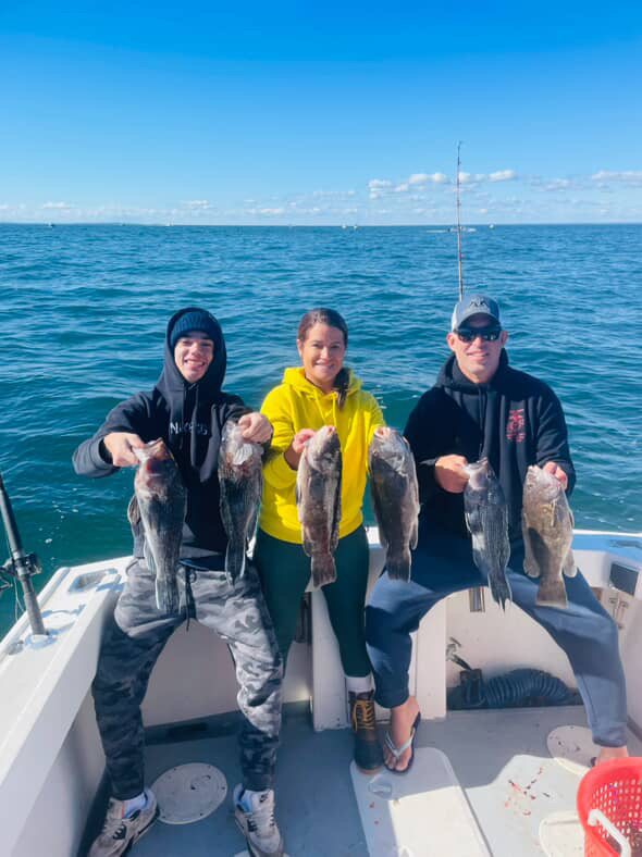 Three anglers, including a young angler, with striped bass on a blue-sky day