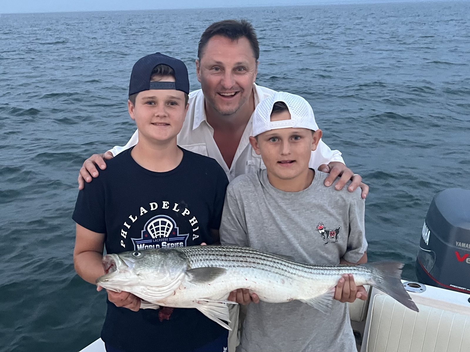 A father and two sons with a big striped bass on a family fishing charter