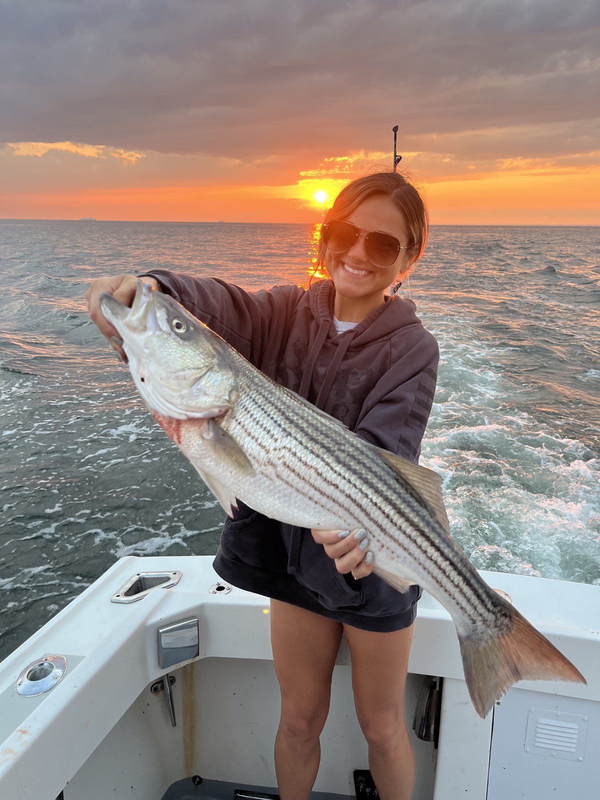 Angler holding a large striped bass at sunset on the Long Island Sound
