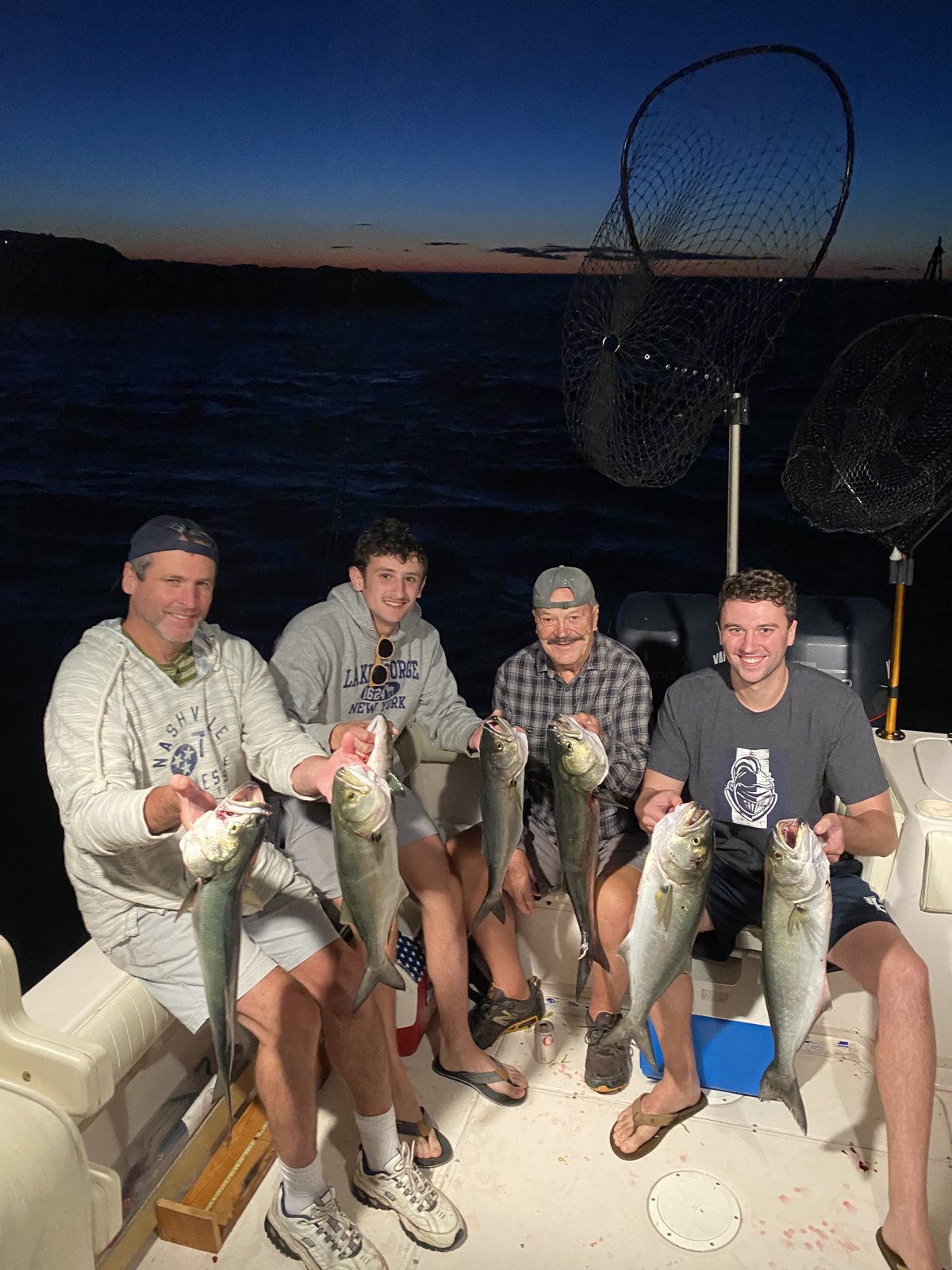 Four anglers with striped bass and a net at dusk on the Long Island Sound
