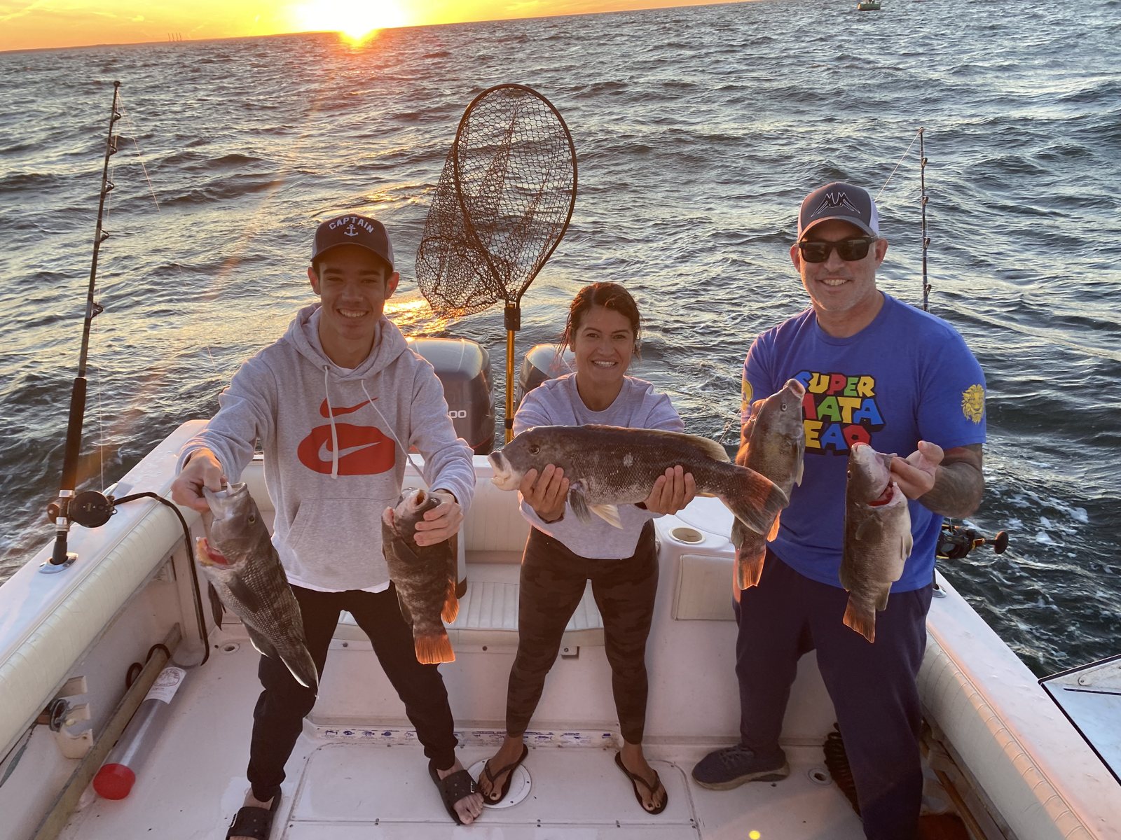 Three anglers holding blackfish at sunset on the Long Island Sound